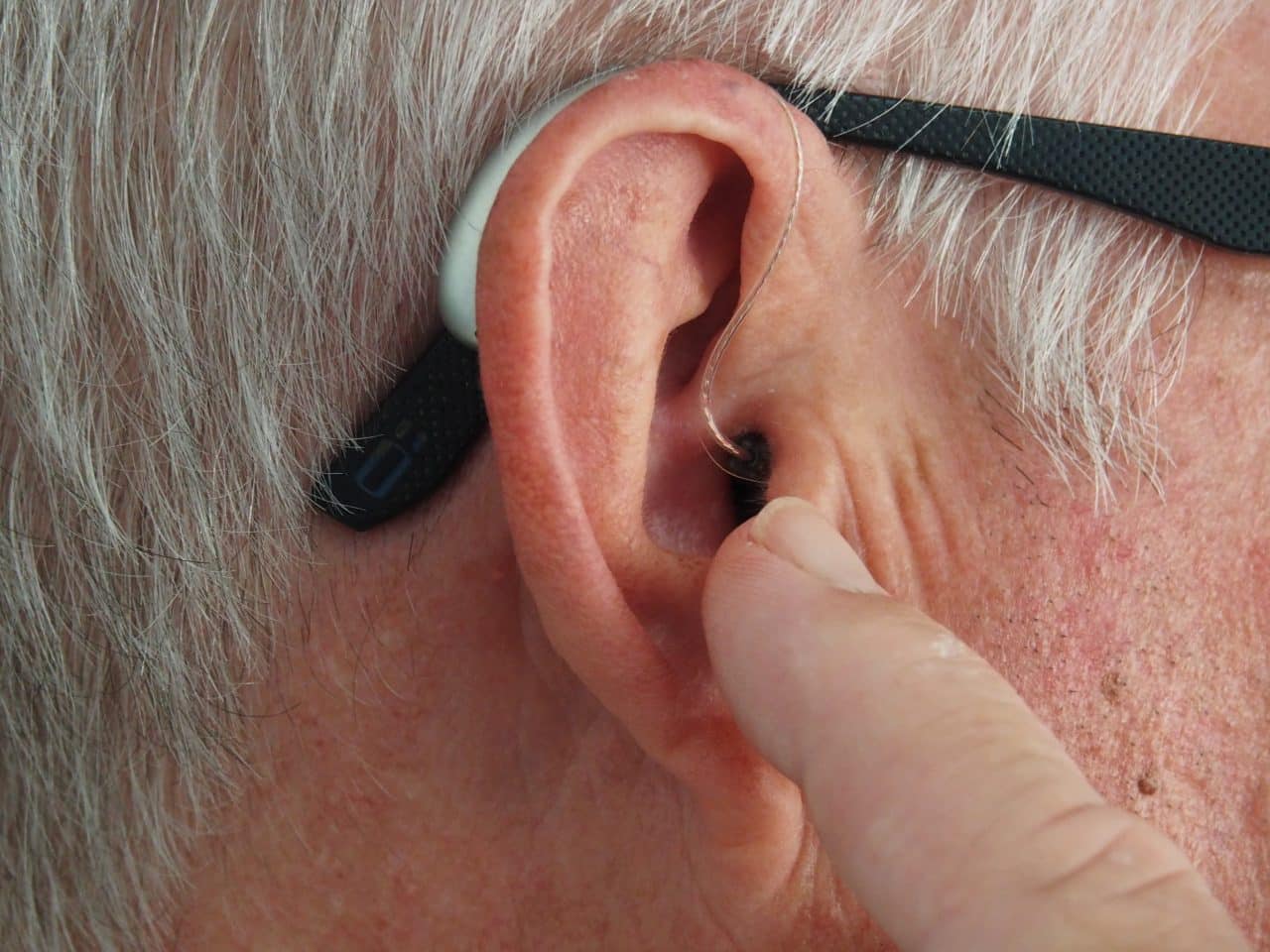 Older man pointing at his hearing aid.