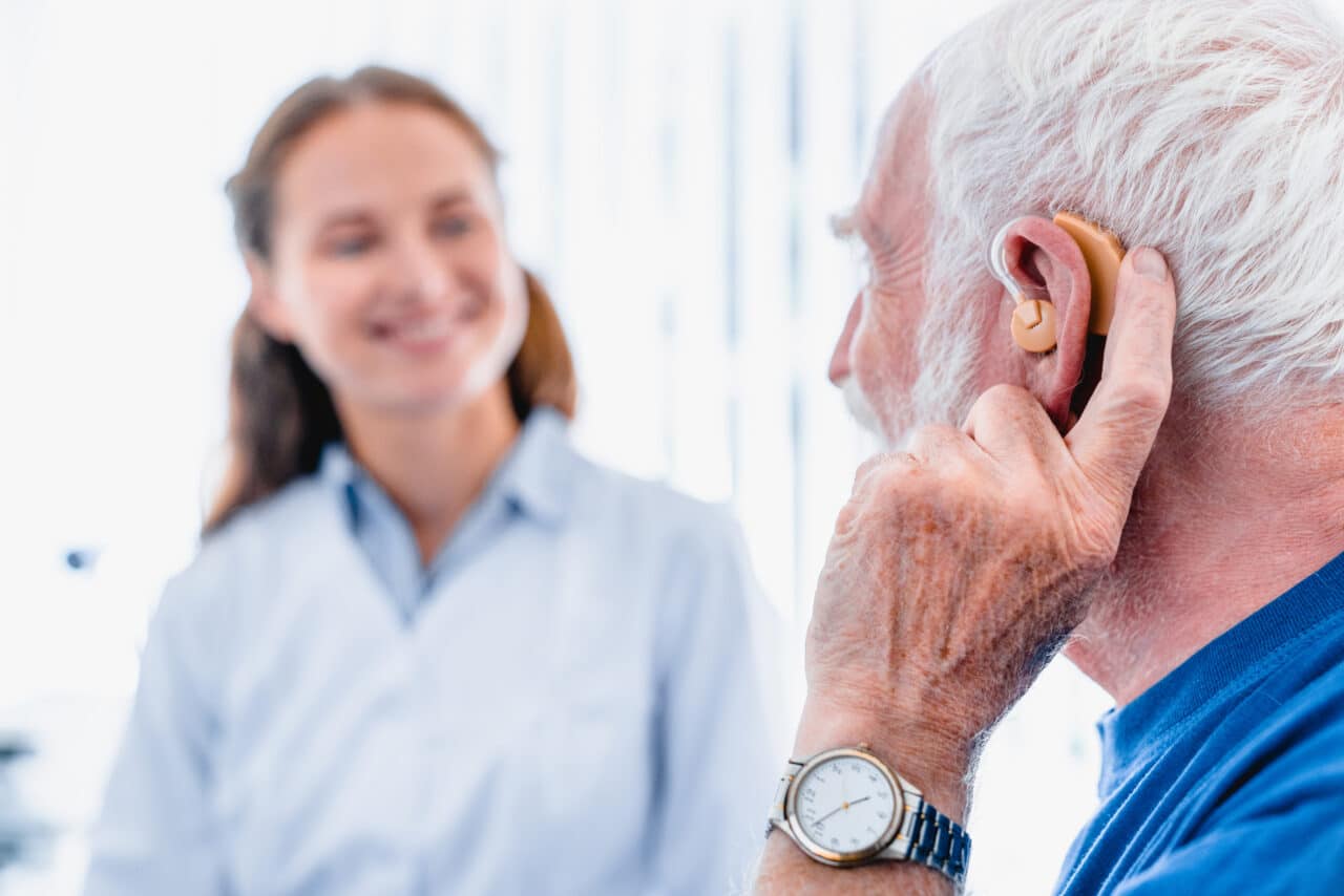 Older male patient with a hearing aid talking to his medical provider.