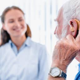 Older male patient with a hearing aid talking to his medical provider.
