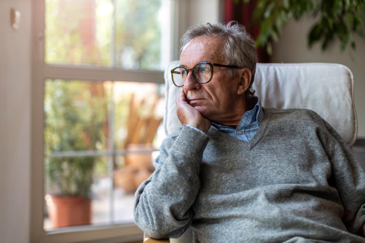 Older man looking out his window at home.