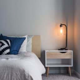 A nightstand with a light on next to a bed.