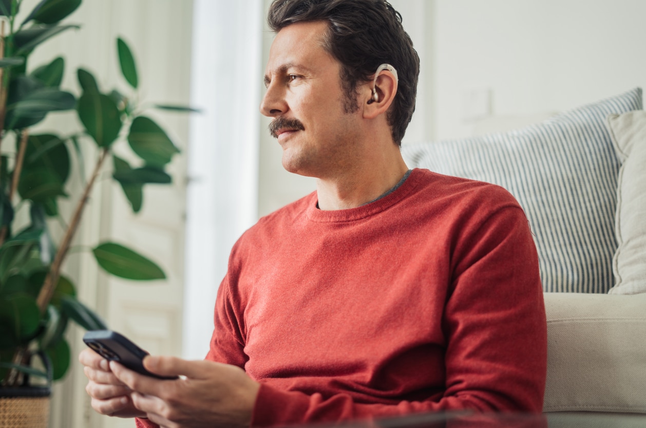 Happy man wearing hearing aids holding a smartphone
