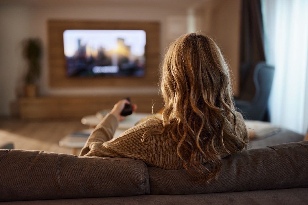 Back view of relaxed woman watching TV at home.